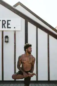 shirtless man doing yoga tree pose standing outside building