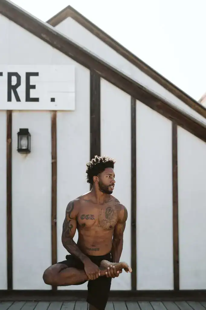 shirtless man doing yoga tree pose standing outside building
