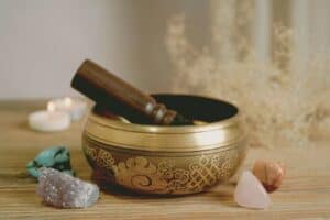 Calming singing bowl with wooden mallet surrounded by crystals and candles, used for meditation and stress relief.