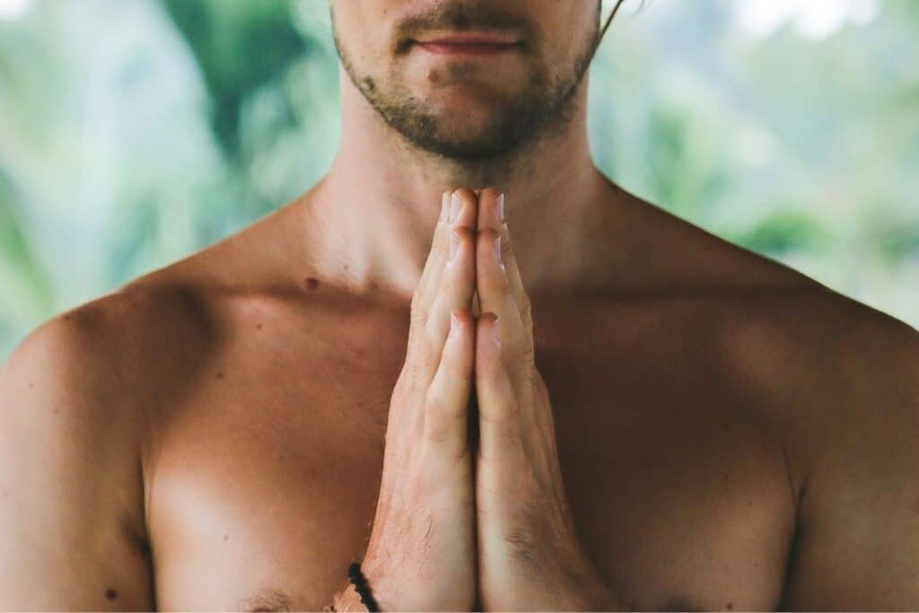 Calm man practicing yoga or meditation, hands in prayer position, close-up of upper body, relaxing environment, mindfulness, wellness, self-care.