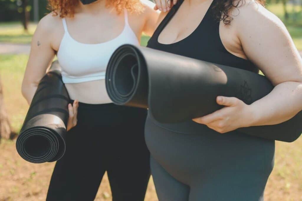 Yoga women holding rolled yoga mats outdoors in a park, promoting mindfulness, relaxation, fitness, and wellness.