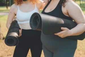 Yoga women holding rolled yoga mats outdoors in a park, promoting mindfulness, relaxation, fitness, and wellness.